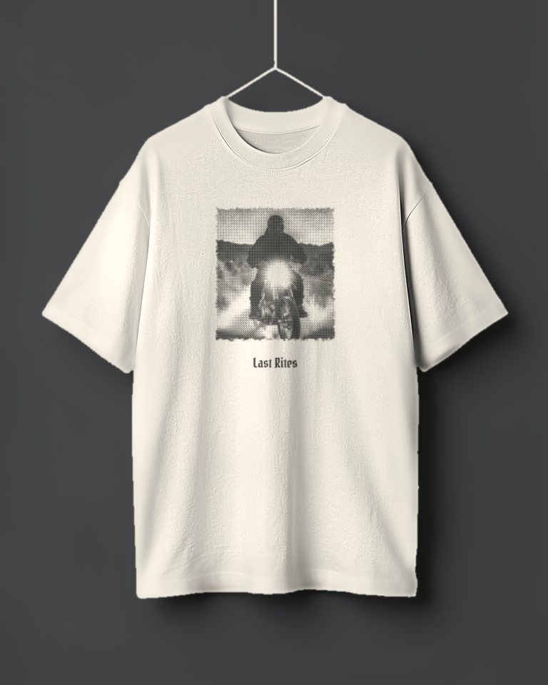 An oversized ecru tee hanging on a thread, printed in faded black with a grainy halftone photo of a rider on a dirt bike at night, headlight on in a cloud of dust, and Last Rites beneath.
